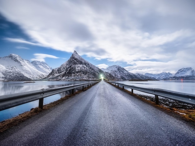 Weg en bergen in de nacht Lofoten-eilanden Noorwegen Asfalt en maanlicht Winterlandschap met nachtelijke hemel Lange belichtingsopname Noorwegen reisbeeld