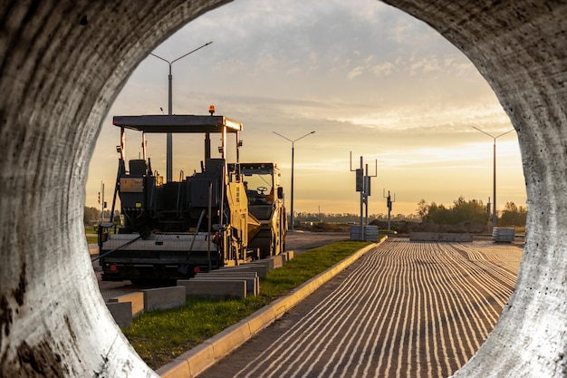 Wegenreparatie en asfaltverharding met een gespecialiseerde machine in de avond tegen de achtergrond van de avondrood