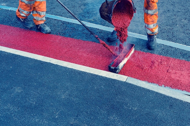 Wegenwerkers die hete rode wegmarkeringsverf aanbrengen op nieuwbouwweg