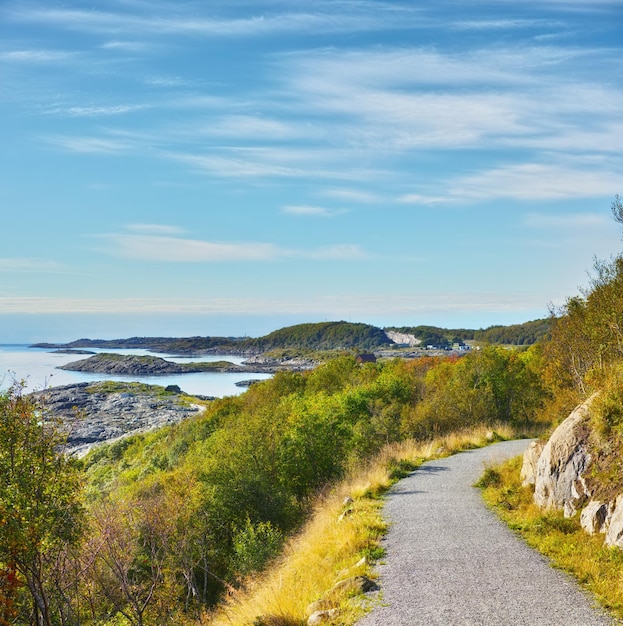 Foto weglandschap en lucht met oceaan in de natuur voor reizen avontuur en bomen met uitzicht op de bergen in noorwegen pad kustlijn en locatie met heuvelweg en omgeving voor vakantie en richting