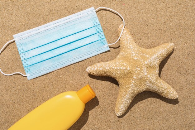 Wegwerp medisch masker, zeester en zonnebrandcrème op het zand