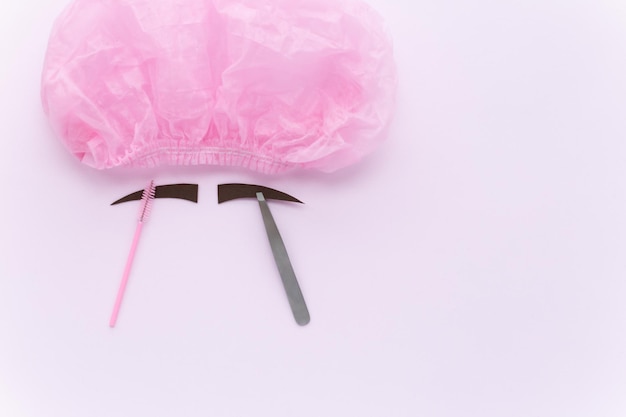Wegwerp medische hoed voor schoonheidssalon klanten en patiënten Decoratieve gesneden bruine wenkbrauwen borstels pincet op een roze achtergrond Platliggende accessoires voor het kleuren, epileren en vormgeven van wenkbrauwen