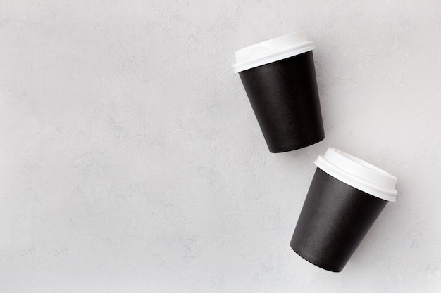 Wegwerp papieren zwarte bekers met gesloten plastic deksel voor koffie om te gaan bovenaanzicht op een grijze achtergrond met kopie ruimte.