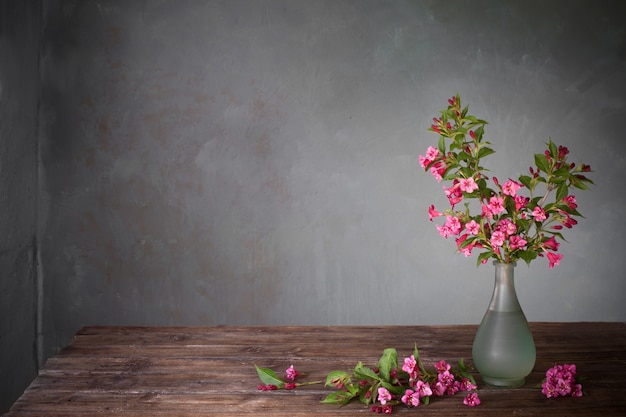 Weigela flowers in glass vase on wooden table