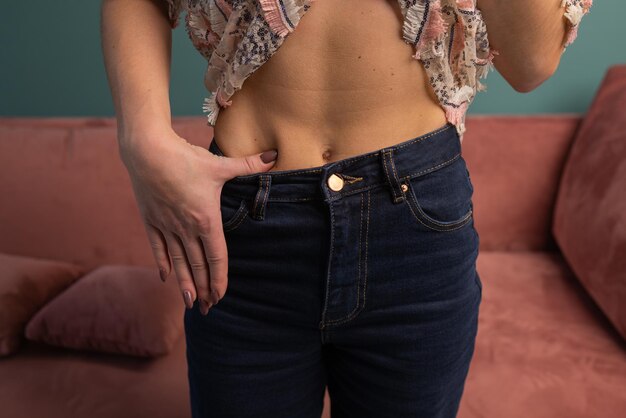 Потеря веса и концепция образа тела. Молодая женщина показывает свою потерю веса и носит старые джинсы. Стройная девушка в больших джинсах показывает, как она худела, когда начала есть здоровую пищу.