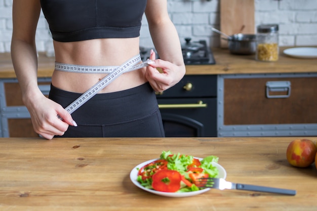 Weight loss concept, woman measures waist in the kitchen