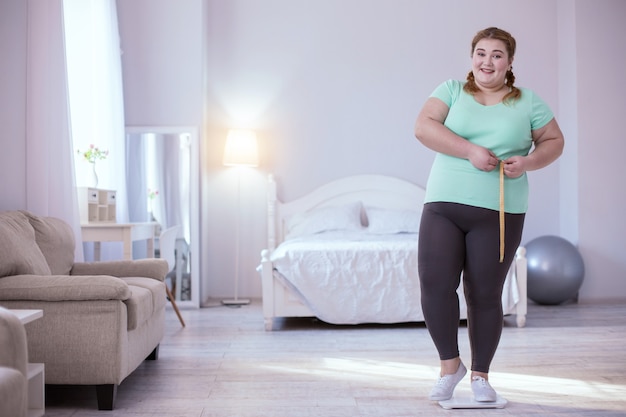 Weight loss. Delighted young woman standing on scales while showing her results