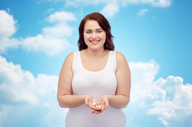 weight loss, diet, slimming, medicine and people concept - happy plus size woman in underwear with pills over blue sky and clouds background