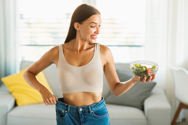 Perdita di peso giovane donna felice che guarda l'insalata di verdure nella ciotola che mostra il risultato positivo del dimagrimento