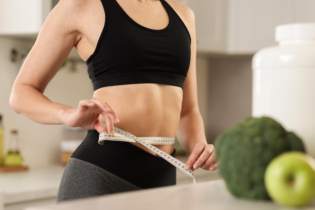 weight loss woman measuring waist with tape in kitchen closeup
