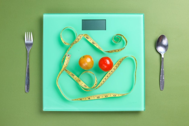 Weight scales cutlery measuring tape and vegetables on green background Diet concept