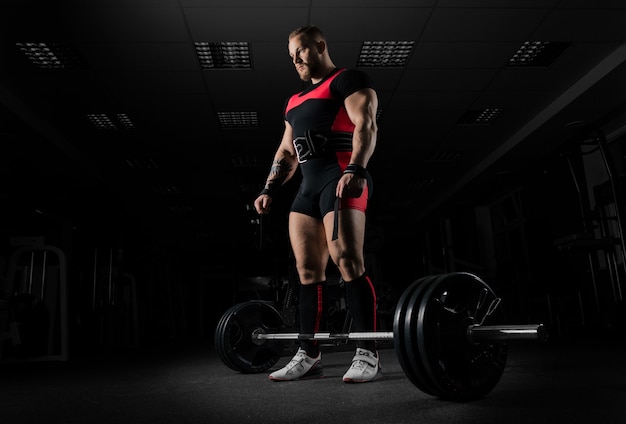 The weightlifter is preparing to perform an exercise called deadlift. He stands directly above the barbell and looks at it.