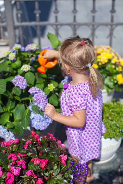 Weinig aardig meisje die bloemen met wateringcan water geven