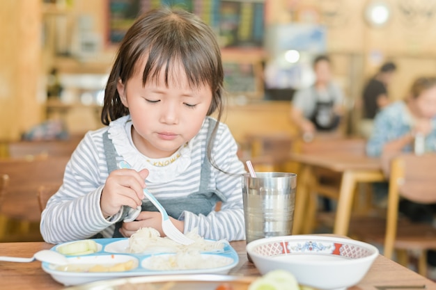 Weinig Aziatisch kindmeisje met ongelukkig gezicht terwijl het hebben van lunch op lijst in restaurant, kieskeurige eter wil niet eten of niet hongerig