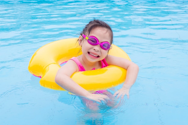 Weinig Aziatisch meisje dat met ring in de pool zwemt