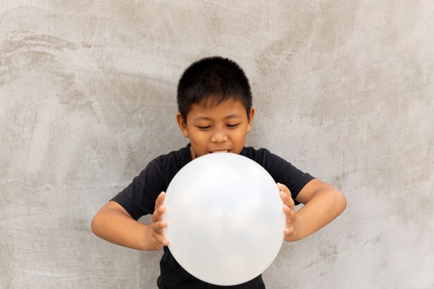 Weinig Aziatische jongen die witte ballons over grijze concrete achtergrond drukt.