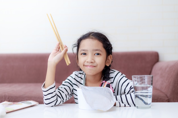 Weinig aziatische meisjeszitting bij witte lijst aan het eten van onmiddellijke noedel