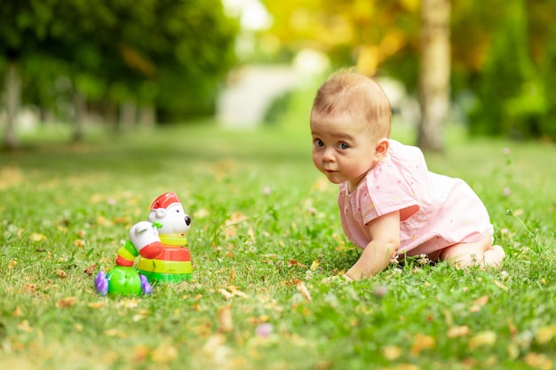 Weinig babymeisje 7 maanden oud die op een groen gazon in een roze Romper spelen