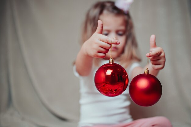 Weinig babymeisje houdt rode kerstballen.