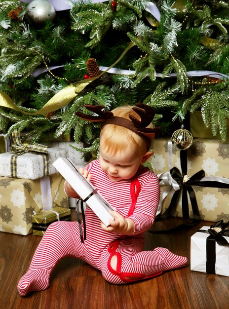 Weinig babymeisje met de giftdoos dichtbij het verfraaien van de kerstboom. Vrolijke tijd.