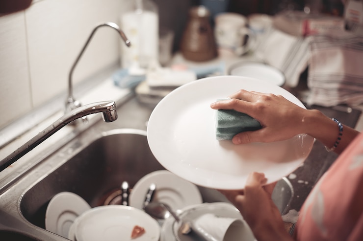 Weinig babymeisje schotel wast in de keuken.