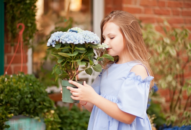 Weinig blond meisje in blauwe kleding met opslag van bloemen de nabijgelegen bloemen