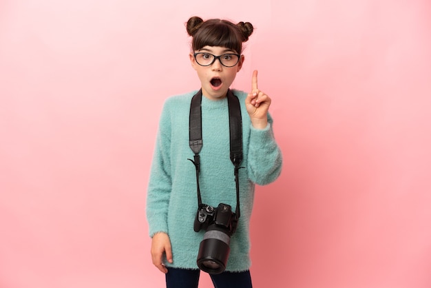 Weinig fotograafmeisje dat op roze achtergrond wordt geïsoleerd die van plan is de oplossing te realiseren terwijl het opheffen van een vinger