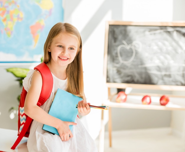 Weinig glimlachend blond meisje dat zich in het schoolklaslokaal bevindt