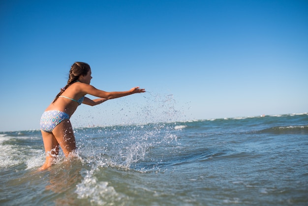 Weinig grappig actief gelukkig meisje spetterend in de lawaaierige zeegolven op een zonnige warme zomerdag. Zee vakantie concept met kinderen.