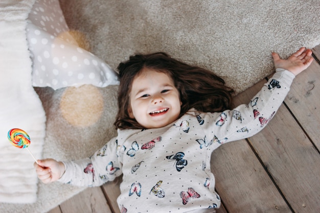 Weinig grappig donkerbruin meisje in comfortabele pyjama's met Lolly op de vloer