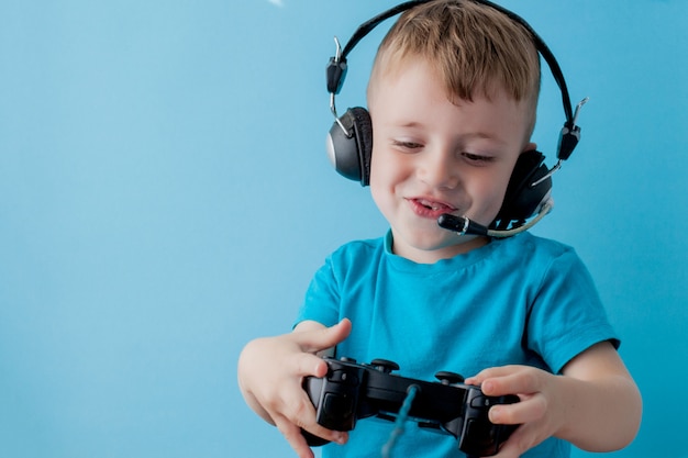 Weinig jong geitjejongen 2-3 jaar die blauwe kleren dragen houdt in hand joystick voor spelen op het blauwe portret van muurkinderen. Mensen jeugd levensstijl concept. Mock up kopie ruimte