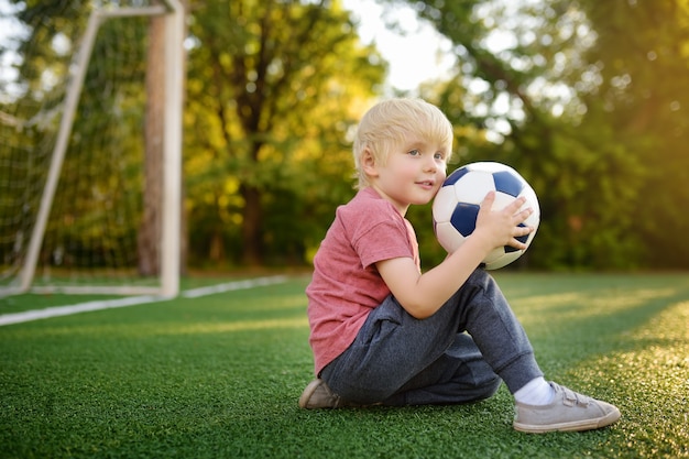 Weinig jongen die pret heeft die een voetbal / een voetbalspel op de zomerdag speelt. actief buiten spel / sport voor kinderen.