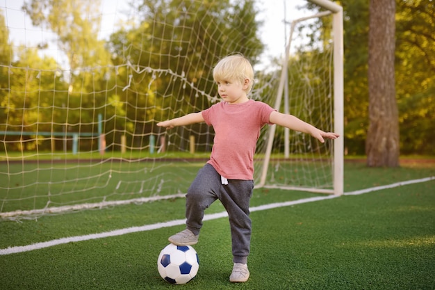 Weinig jongen die pret heeft die een voetbal / een voetbalspel op de zomerdag speelt.