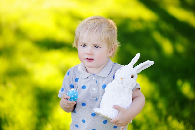 Weinig jongen die voor paasei in de lentetuin jaagt op Pasen-dag. Schattig klein kind met traditionele bunny feest vieren