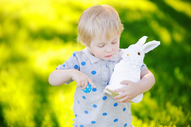 Weinig jongen die voor paasei in de lentetuin jaagt op Pasen-dag. Schattig klein kind met traditionele bunny feest vieren