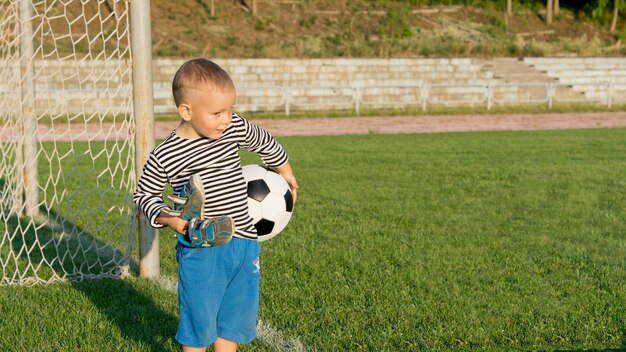 Weinig jongen die voor th doelen wacht om te voetballen met zijn schoenen in de ene hand en een voetbal in de andere