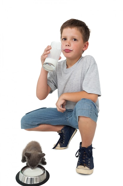 Weinig jongen en grijs katje allebei die melk drinken