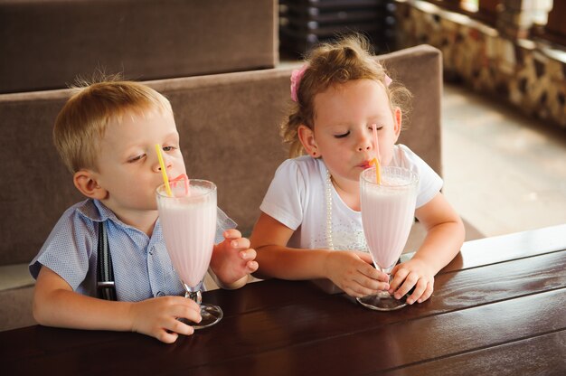 Weinig jongen en meisje die milkshakes in een koffie in openlucht drinken.