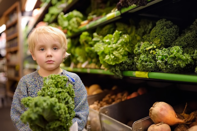 Weinig jongen in een supermarkt die verse organische boerenkool kiezen