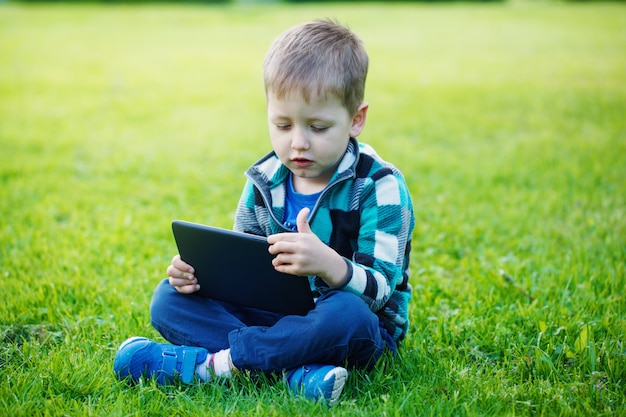 Weinig jongen met tablet zit op het gras