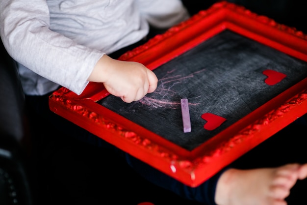 Weinig jongenszitting op de leunstoel met rood ontworpen beeld op de Valentijnskaartendag