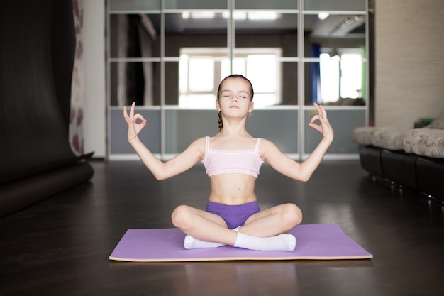 Weinig Kaukasische meisjeszitting op mat in yoga stelt en mediterend.