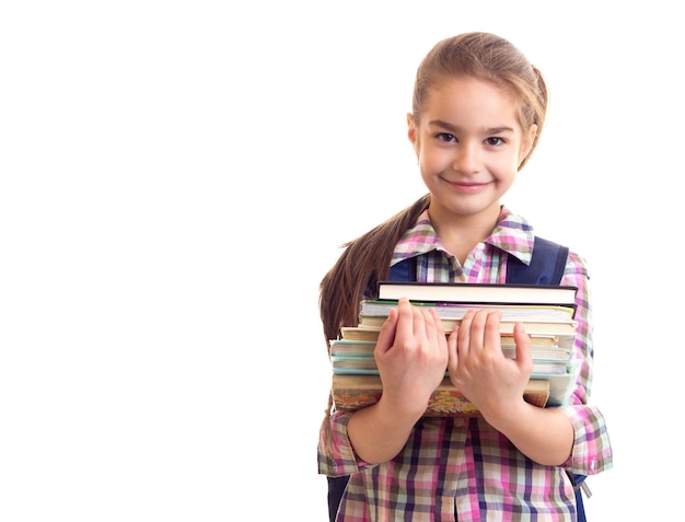 Weinig lachend schoolmeisje met boeken in handen die in de camera kijken naar witte achtergrond.