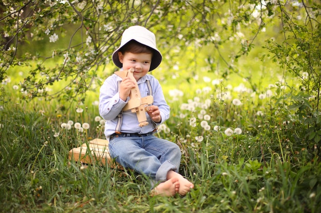 Weinig leuke blonde jongen die met een houten vliegtuig in het de zomerpark spelen op het gras op een zonnige dag