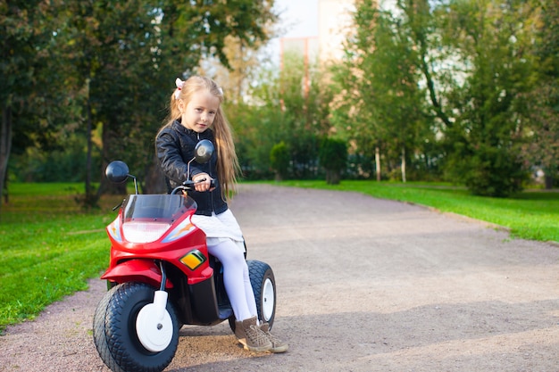 Weinig mooi rotsmeisje in leerjasjezitting op haar stuk speelgoed motorfiets