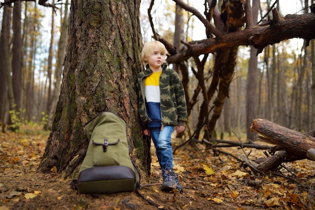 Foto weinig padvinder met grote rugzak heeft rust dichtbij grote boom in wild bos op de herfstdag.