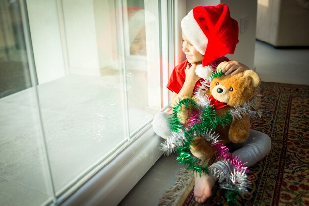 Weinig schattige jongen in rode dop van de kerstman viert Kerstmis