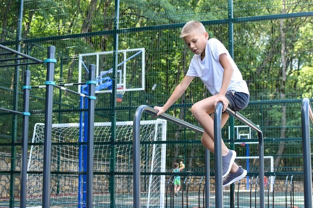 Weinig sportman op de horizontale balk op speelplaats. kindersport voor de gezondheid