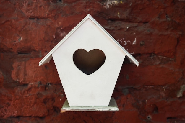 Weinig wit vogelhuisje met het gat van het hartsymbool dat van rode bakstenen muur hangt. dwergpapegaaien naar huis, valentijn cadeau-concepten