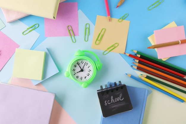 Wekker, boeken en briefpapier op pastelkleurenachtergrond van kleurrijk papier, terug naar school